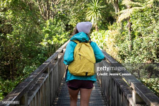 rear view of a woman wearing a backpack walking on a bridge through nature - new zealand yellow stock pictures, royalty-free photos & images