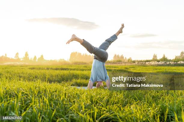 young man doing yoga in the field at sunset. summer day, wellness concept. - acrobatic yoga stock-fotos und bilder