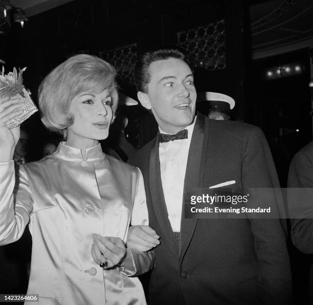 German actress Margit Saad, wearing a satin high-neck jacket waving a small purse her right hand, with British designer, producer and opera...