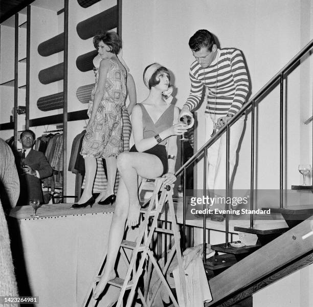 British fashion model Grace Coddington having her glass topped up by a man in a hooped top, as Coddington sits at the top of a step ladder during a...