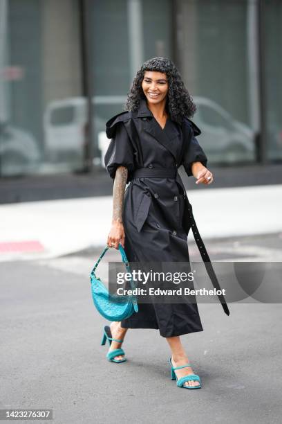 Guest wears a black long belted trench coat, a flashy blue shiny leather crocodile print pattern handbag, flashy blue shiny leather and fluffy strap...