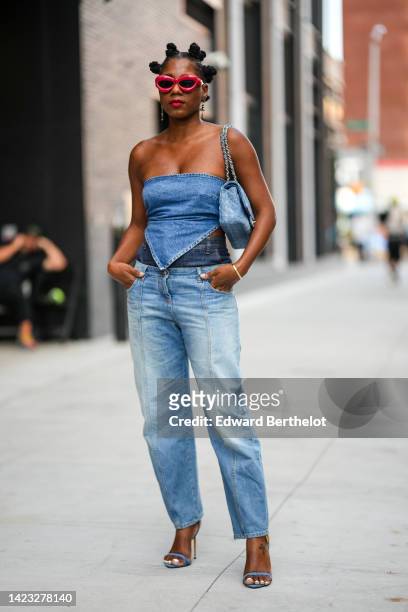 Guest wears red sunglasses, gold logo pendant earrings from Chanel, a blue denim Timeless shoulder bag from Chanel, a blue denim shoulder-off /...