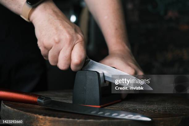 woman is sharpening a kitchen knife using knife sharpener in domestic kitchen - sharpening stock pictures, royalty-free photos & images