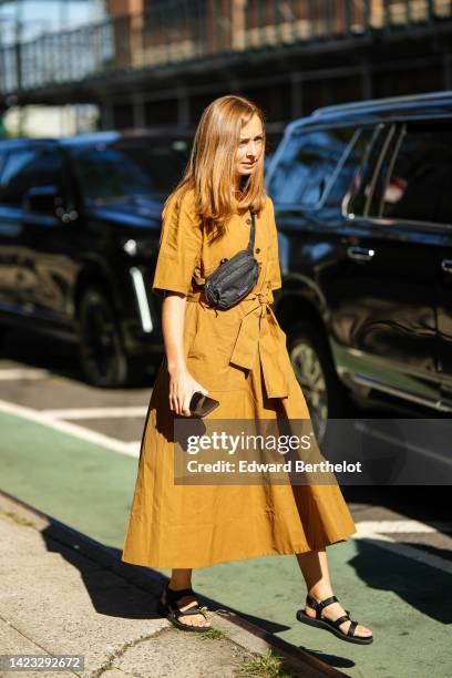 Guest wears a yellow mustard short sleeves / buttoned / belted long dress, a black nylon fanny pack bag from Patagonia, black strappy sandals ,...