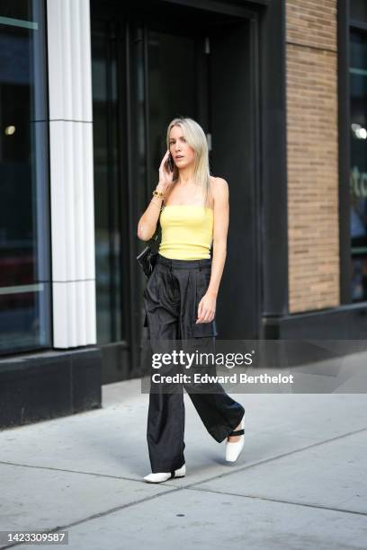 Guest wears a yellow shoulder-off top, a black shiny varnished leather shoulder bag, black large cargo pants, white shiny leather ballerinas, outside...