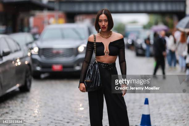 Tiffany Hsu seen wearing a gold large chain necklace, a black V-neck / shoulder-off / long sleeves cropped top, a black shiny leather Chanel 22 large...