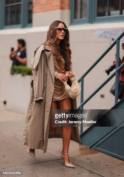 Tamara Kalinic seen wearing beige and brown futurist sunglasses, a gold wrap short dress, a beige long trench coat, a beige Bottega Veneta handbag, a...