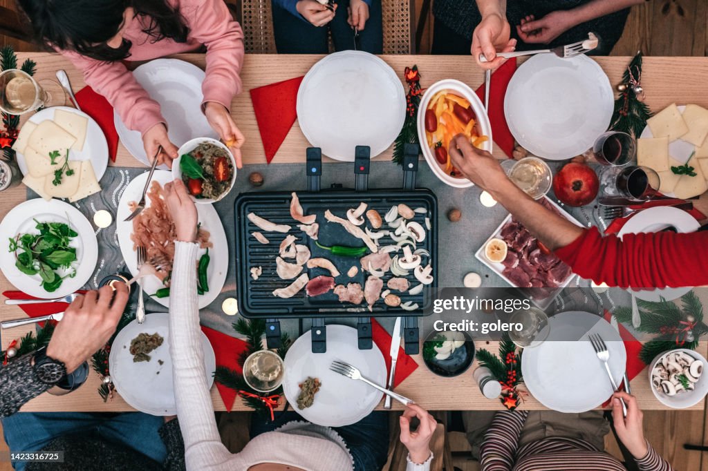 Family preparing various dishes on raclette grill on wooden table