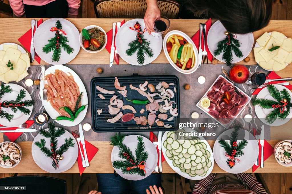 Family preparing various dishes on raclette grill on wooden table