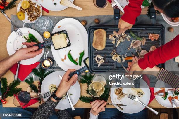 family preparing various dishes on raclette grill on wooden table - raclette stock pictures, royalty-free photos & images
