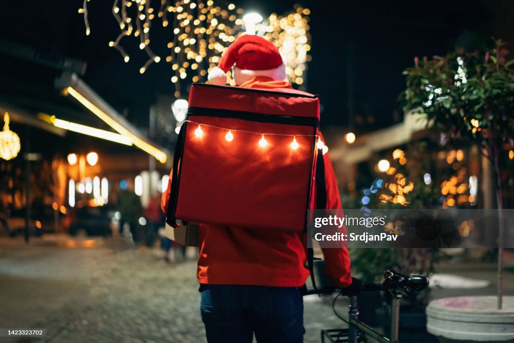 Unrecognizable delivery person pushing bicycle through city, decorated in Christmas spirit
