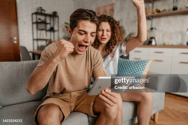 young couple watching a sports game on tablet and rooting for their team - sport tablet stock pictures, royalty-free photos & images