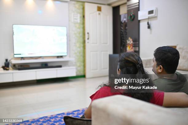 couple sitting down on the carpet floor and watching television show - indian living room stock pictures, royalty-free photos & images