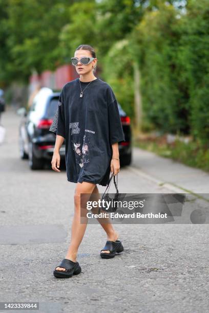 Guest wears silver sunglasses, a silver chain pendant necklace from Louis Vuitton, a black with white inscription print pattern oversized t-shirt...