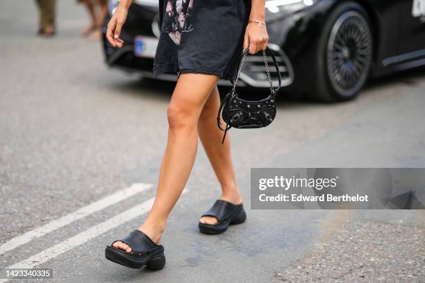 Guest wears a black with white inscription print pattern oversized t-shirt from Balenciaga, a black shiny leather nailed / studded small Cagole...