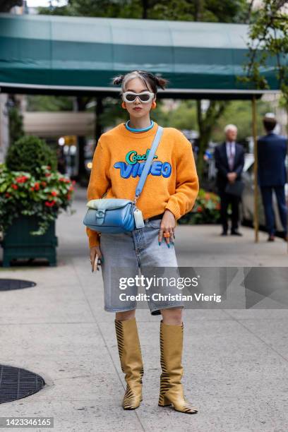 Guest wearing blue Coach bag, orange knit, denim jeans outside Coach on September 12, 2022 in New York City.