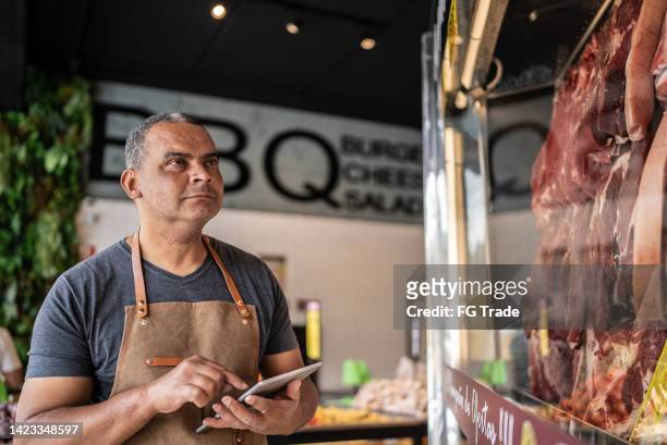 business owner with digital tablet taking inventory in a butcher's shop - slagerij stockfoto's en -beelden