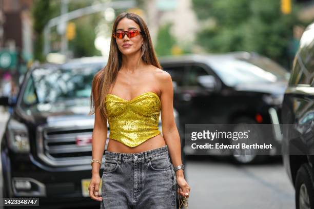 Tamara Kalinic wears red sunglasses, gold earrings, a gold shiny sequined heart shoulder-neck / cropped top, silver watch, a gold Clash bracelet from...