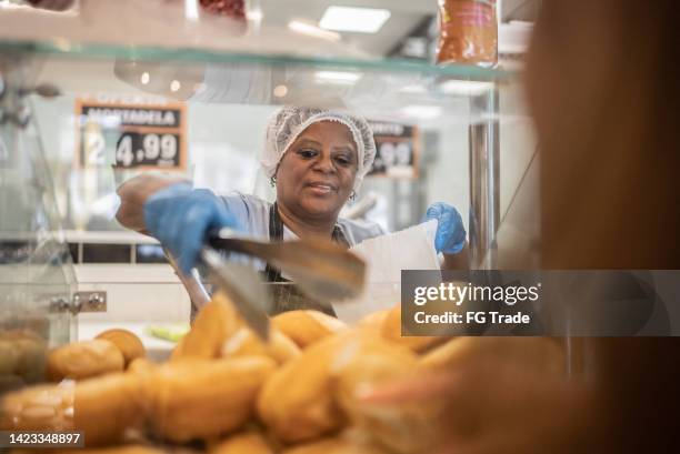 employee getting some bread to customer in a bakery - haarnet stockfoto's en -beelden