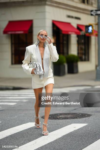 Leonie Hanne wears silver and crystal sunglasses, large crystals pendant fringed earrings, a white latte oversized / shoulder-pads blazer jacket...