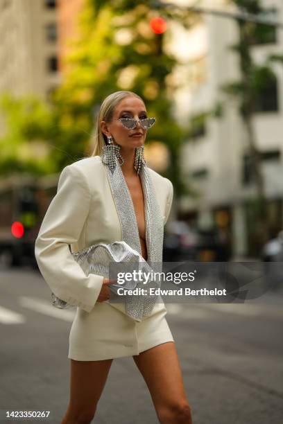 Leonie Hanne wears silver and crystal sunglasses, large crystals pendant fringed earrings, a white latte oversized / shoulder-pads blazer jacket...