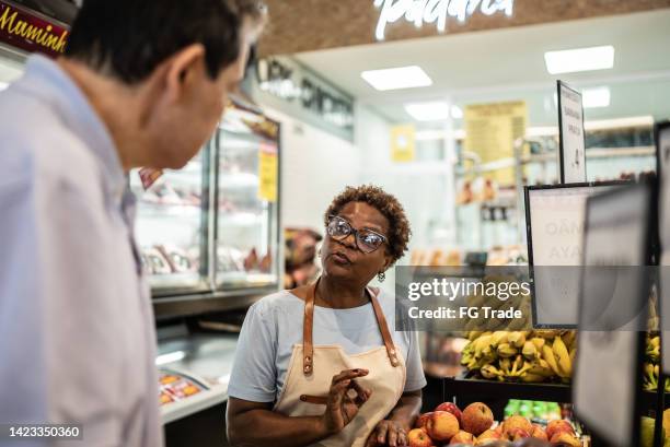 saleswoman helping a customer in a supermarket - corner shop stock pictures, royalty-free photos & images