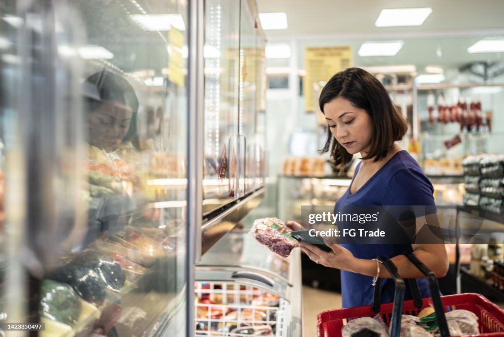 Mid adult woman using the mobile phone buying groceries in a supermarket