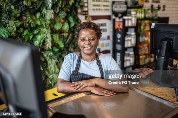 portrait of a senior woman cashier working in a market - cornershop stock pictures, royalty-free photos & images