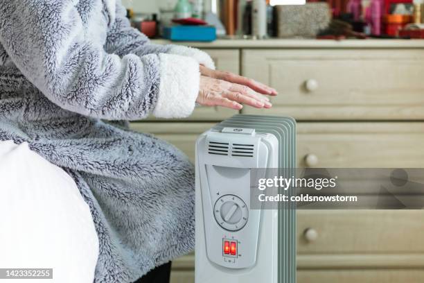 senior woman warming her hands over electric heater at home - copy space 個照片及圖片檔