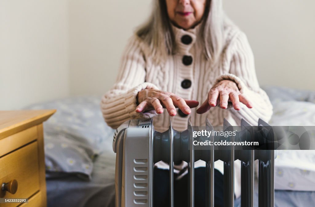 Mujer mayor calentando sus manos sobre calentador eléctrico en casa