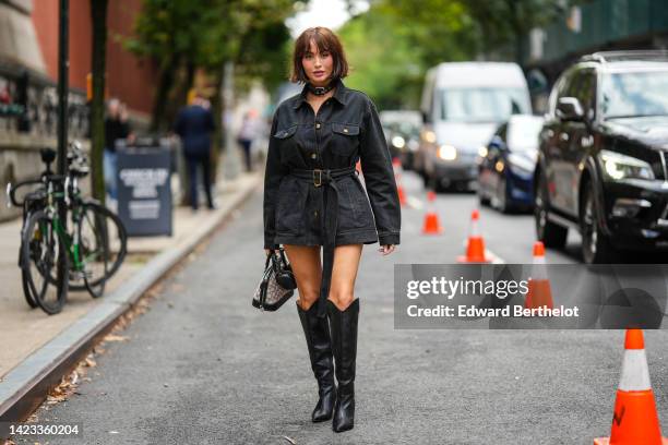 Taylor Lashae wears a black large shiny leather belt necklace, a black oversized denim belted jacket, a black shiny leather handbag, a black shiny...