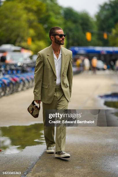 Pelayo Diaz wears black sunglasses, a gold chain pendant necklace, a white shirt, a green oversized blazer jacket, matching green suit pants, a beige...