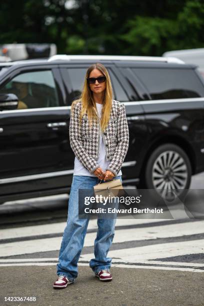 Charlotte Groeneveld wears black sunglasses, a white t-shirt, a black and white tweed checkered print pattern jacket, blue denim large pants, a beige...