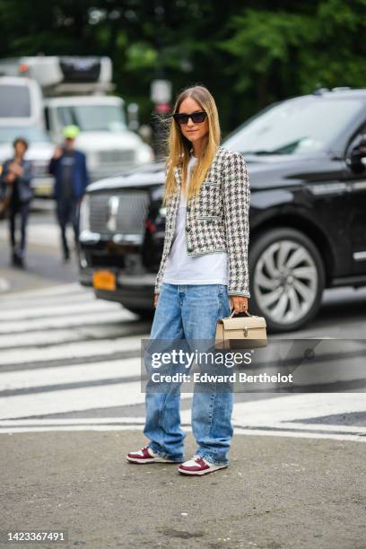 Charlotte Groeneveld wears black sunglasses, a white t-shirt, a black and white tweed checkered print pattern jacket, blue denim large pants, a beige...