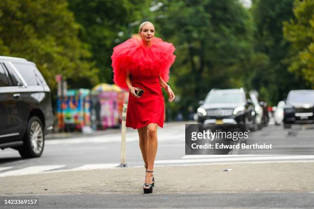 Leonie Hanne wears gold earrings, a red short dress with oversized ruffled tulle shoulder, a gold Juste Un Clou bracelet from Cartier, a gold and...