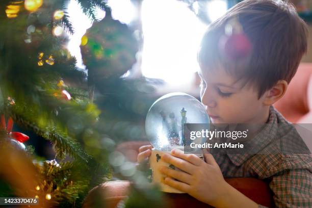 süßer kleiner junge im pyjama, der an heiligabend zu hause mit einer schneekugel spielt - snow globe stock-fotos und bilder