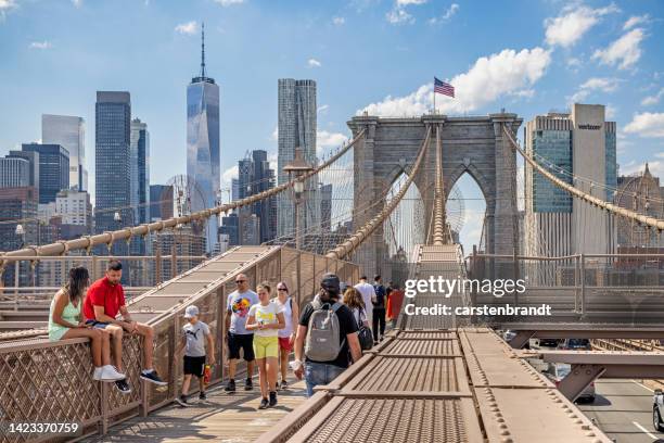 menschen, die auf der brooklyn bridge mit der skyline von manhattan im hintergrund spazieren gehen - touristen brooklyn bridge stock-fotos und bilder