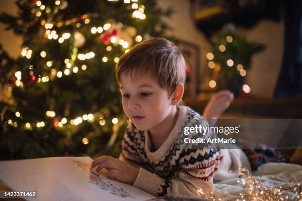 little boy reading a book near christmas tree - bedtime story book stock pictures, royalty-free photos & images