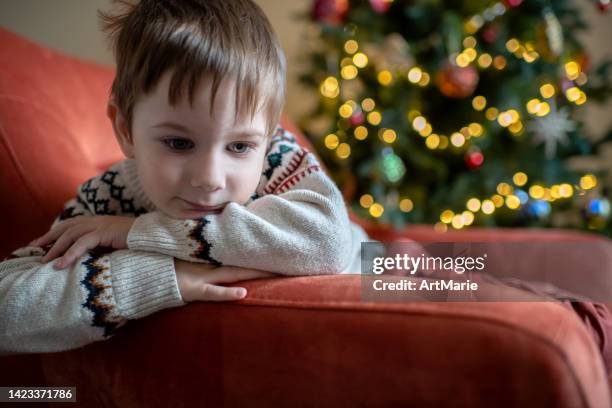 little boy sitting on an arm-chair on christmas holidays - christmas loneliness stock pictures, royalty-free photos & images