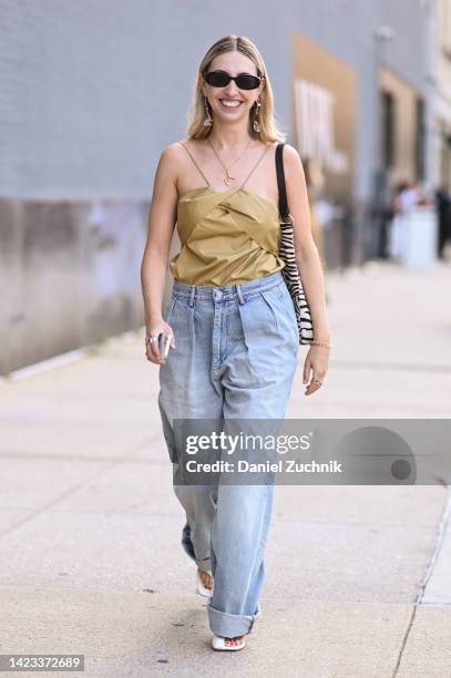 Madeline Harper Fass is seen wearing a green top, light blue jeand and black sunglasses with gold pearl earrings outside the Veronica Beard show...