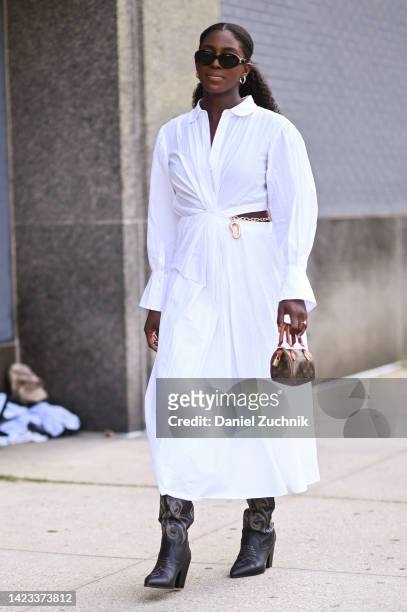 Guest is seen wearing a white dress, black boots and Louis Vuitton mini bag outside the Veronica Beard show during New York Fashion Week S/S 2023 on...