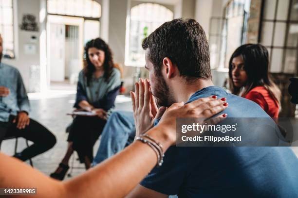 la gente está consolando a un hombre durante una sesión de terapia de grupo - alcohólicos anónimos fotografías e imágenes de stock
