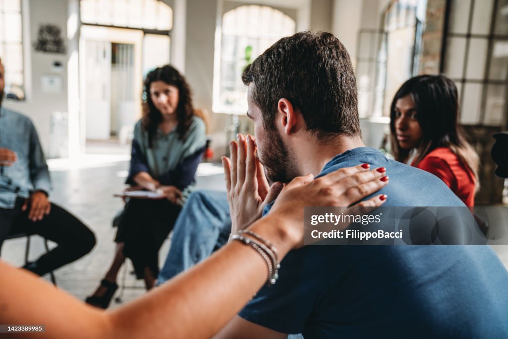 People are comforting a man during a group therapy session