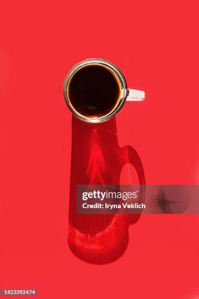 glass cup with aromatic morning coffee or tea and a long shadow from the cup on coral red color background. - red mug stock pictures, royalty-free photos & images