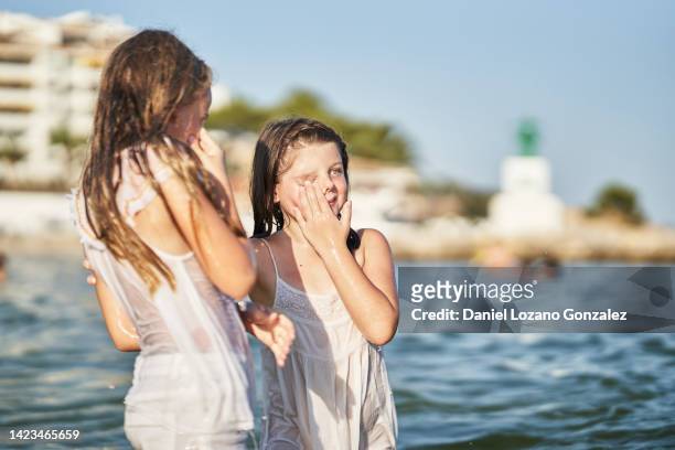 two girls dressed in clothes and wet while standing on the seashore at the beach. - girls in wet dresses stock-fotos und bilder