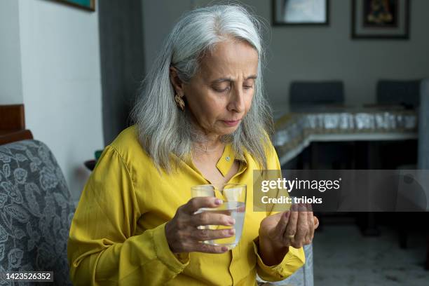 senior woman taking pill - pillen nemen stockfoto's en -beelden