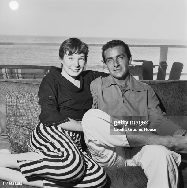 American actress and singer Shirley MacLaine, wearing a black sweater and striped trousers, and her husband, American businessman and film producer...