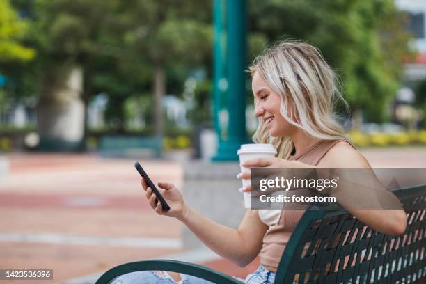 cheerful young woman enjoying a takeaway coffee and texting with friends - centenial olympic park stock pictures, royalty-free photos & images