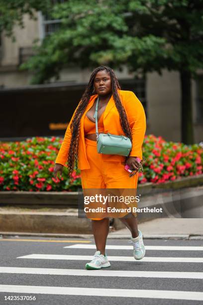 Guest wears gold earrings, a pale green shiny leather crossbody bag, a neon orange blazer jacket, matching neon orange V-neck / cropped top, neon...