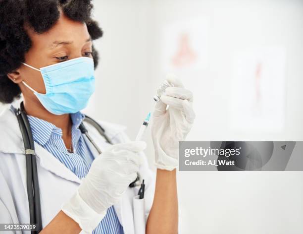 doctor wearing face mask filling a syringe with vaccine in clinic - antibiotic injection stock pictures, royalty-free photos & images